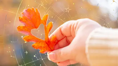 Ein Blatt mit einem ausgestanzten Herz wird vor einen Hintergrund mit goldenen Verzierungen gehalten. - Foto: Collage mit iStock (Victor Golmer) und Astrowoche.de