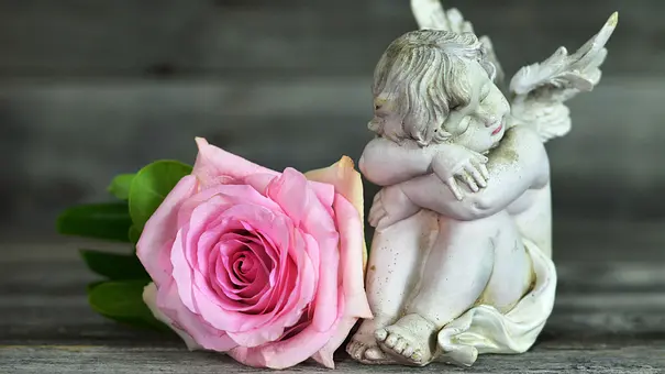 Kleine Engelstatue neben einer pinken Rose - Foto: izzzy71 / AdobeStock Kleine Engelstatue neben einer pinken Rose - Foto: izzzy71 / AdobeStock