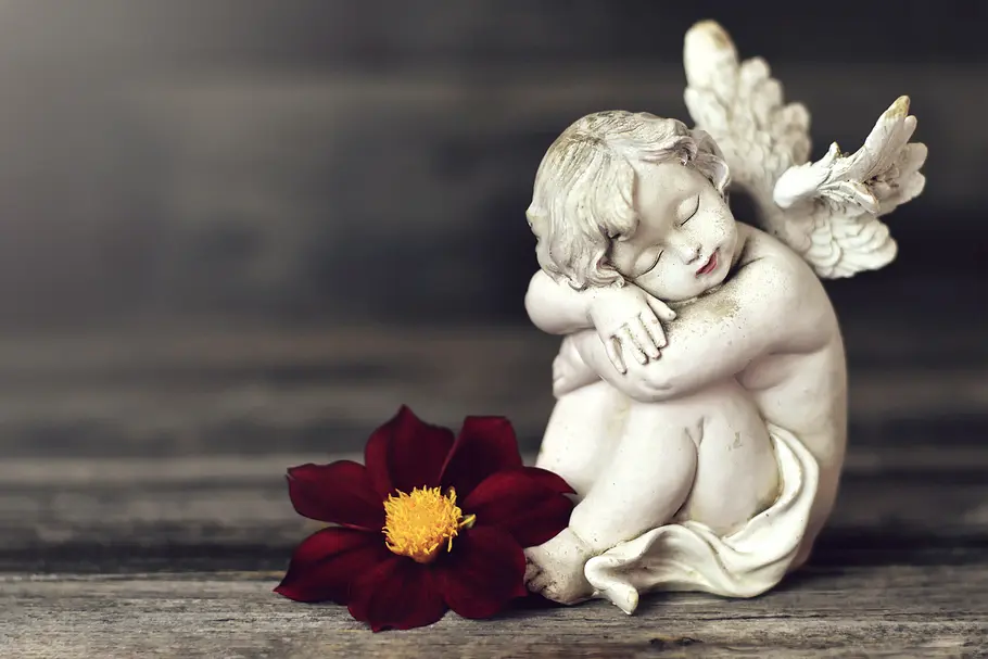 Kleine Engelstatue sitzt vor einer roten Blüte