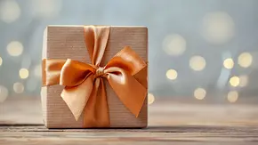Geburtstagsgeschenk mit Orangener Schleife und braunem Geschenkpapier - Foto: Volha Zaitsava / AdobeStock