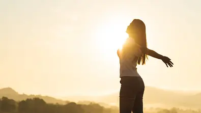 Silhouette einer Frau, die ihre Arme glücklich in die Sonne ausbreitet - Foto: Siam / AdobeStock