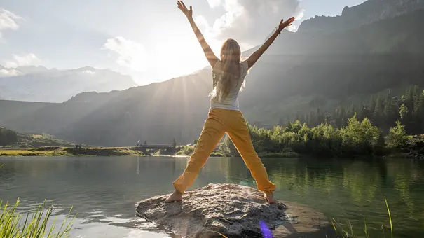 Junge Frau rümpft sich bei Sonnenaufgang auf Felsen über Alpensee - Foto: Mystockimages / iStock Junge Frau rümpft sich bei Sonnenaufgang auf Felsen über Alpensee - Foto: Mystockimages / iStock