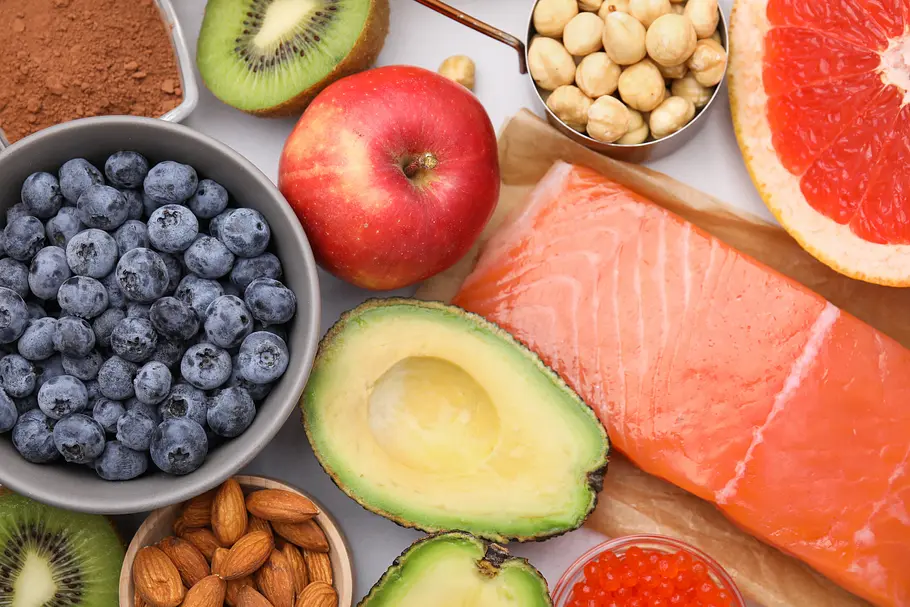 Verschiedenes Obst, Gemüse, Nüsse und Lachs liegen auf einem Tisch.