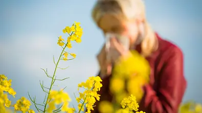Frau steht mit einem Taschentuch hinter gelben Blüten - Foto: Sandor Jackal / AdobeStock