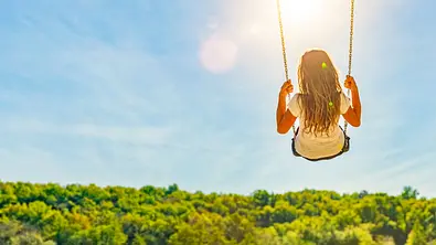 Frau sitzt auf einer Schaukel vor einem grünen Wald - Foto: by-studio / AdobeStock Frau sitzt auf einer Schaukel vor einem grünen Wald - Foto: by-studio / AdobeStock