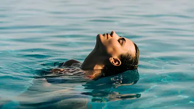 Eine Frau treibt mit geschlossenen Augen und zurückgelegtem Kopf auf dem Rücken im türkisblauen Wasser eines Pools. - Foto: F8 \ Suport Ukraine/AdobeStock Eine Frau treibt mit geschlossenen Augen und zurückgelegtem Kopf auf dem Rücken im türkisblauen Wasser eines Pools. - Foto: F8 \ Suport Ukraine/AdobeStock
