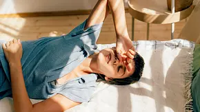 Frau liegt auf ihrem Bett und liegt ihre Hand auf ihrer Stirn ab - Foto:  Ilona / AdobeStock