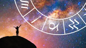 Frau steht mit ausgestreckten Armen auf einem Hügel vor einem bunten galaktischen Hintergrund mit einem halben Sternzeichenkreis - Foto: Collage mit AdobeStock (PRASERT; vectorfusionart) und Astrowoche.de