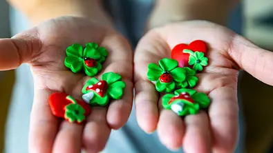 Frau hält verschiedene Glücksbringer (Kleeblätter, Herzen, Fliegenpilze, Marienkäfer) in den Händen. - Foto:  Milan / AdobeStock