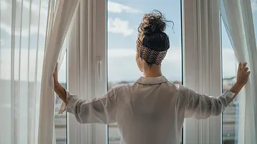 Frau öffnet die Vorhänge und blickt aus dem Fenster - Foto: iStock/Milan Markovic Frau öffnet die Vorhänge und blickt aus dem Fenster - Foto: iStock/Milan Markovic