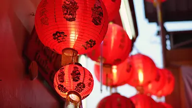 Das Bild zeigt rote chinesische Papierlampen mit schwarzen Schriftzeichen, die festlich nebeneinander hängen. - Foto: bunyarit/iStock Das Bild zeigt rote chinesische Papierlampen mit schwarzen Schriftzeichen, die festlich nebeneinander hängen. - Foto: bunyarit/iStock