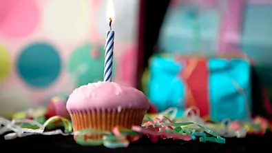 Muffin mit rosanem Zuckerguss und einer Geburtstagskerze auf einem Geburtstagstisch. - Foto: Wavebreakmedia / iStock