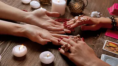 Zwei Hände, aus denen gelesen wird, umgeben von Kerzen. - Foto: Africa Studio/AdobeStock