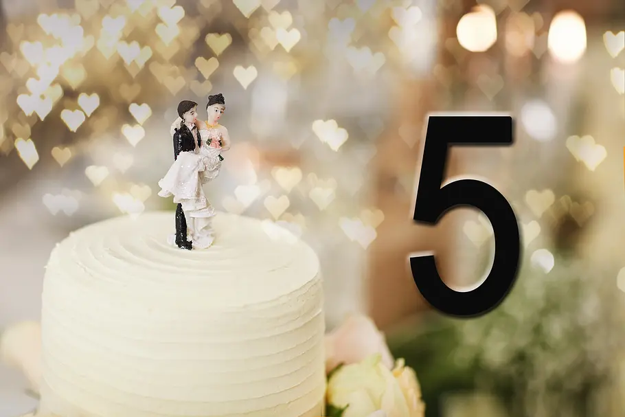 Dekofiguren eines Brautpaares auf einer Hochzeitstorte vor der Zahl 5