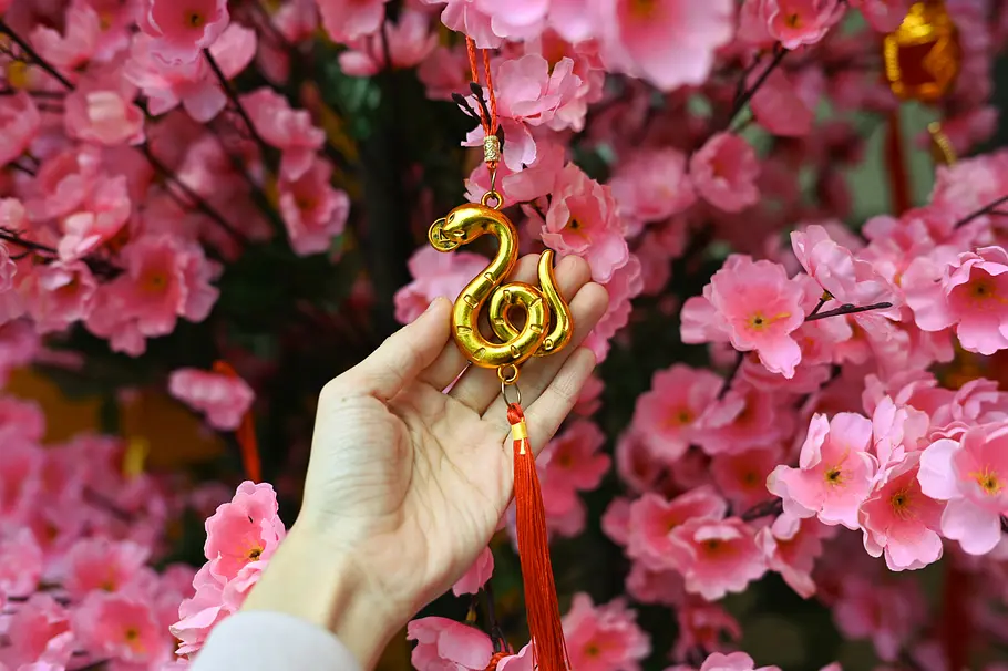 Für diese 4 chinesischen Sternzeichen wird der April 2025 paradiesisch schön! Hand hält goldenen Schlangenanhänger inmitten von pinken Kirschblüten