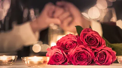 Rote Rosen im Vordergrund, zwei Hände, die sich greifen im Hintergrund - Foto: iStock/kieferpix