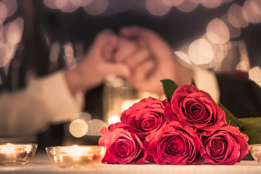 Das Horoskop für den Valentinstag 2025 Rote Rosen im Vordergrund, zwei Hände, die sich greifen im Hintergrund