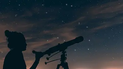 Frau guckt mit Teleskop in den Nachthimmel - Foto: Allexxandar/iStock