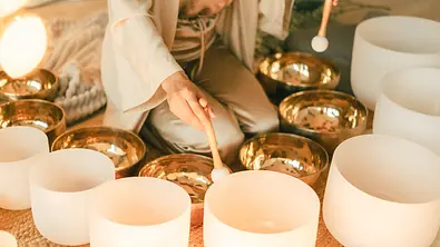 Eine Frau sitzt vor einem Halbkreis aus Klangschalen - Foto: CHEBOTKEVICH / iStock Eine Frau sitzt vor einem Halbkreis aus Klangschalen - Foto: CHEBOTKEVICH / iStock