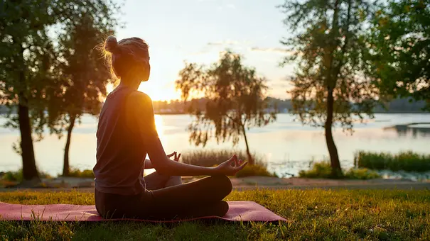 Frau sitzt im Lotussitz an einem See in der Sonne - Foto: Svitlana / AdobeStock