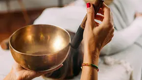 Frau mit roten Fingernägeln hält eine Klangschale bei einer Massage - Foto: Microgen / AdobeStock