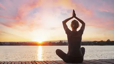 Frau sitzt in Meditationspose vor einem See im Sonnenaufgang - Foto: Song_about_summer / AdobeStock