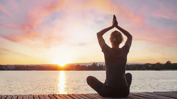 Frau sitzt in Meditationspose vor einem See im Sonnenaufgang - Foto: Song_about_summer / AdobeStock