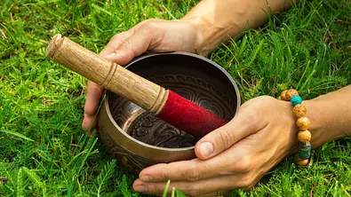 Die Hände einer jungen Frau auf tibetischen Klangschale mit Holzstab auf dem Rasen - Foto: iStock/undefined undefined Die Hände einer jungen Frau auf tibetischen Klangschale mit Holzstab auf dem Rasen - Foto: iStock/undefined undefined