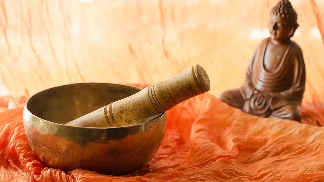Eine Klangschale und ein Buddha aus Holz auf einem orangenen Tuch - Foto: vasanty / AdobeStock Eine Klangschale und ein Buddha aus Holz auf einem orangenen Tuch - Foto: vasanty / AdobeStock