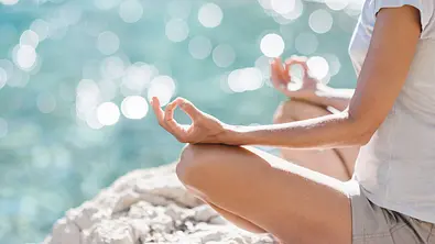 Frau sitzt in einer Meditationspose vorm Meer - Foto: kite_rin / AdobeStock