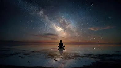 Person meditiert auf einem spiegelnden Untergrund vor einem Sternenhimmel - Foto: Volodymyr Shcherbak / AdobeStock