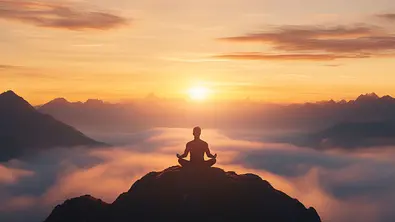 Mann sitzt meditierend auf einem Hügel umgeben von Wolken - Foto: Akash / AdobeStock