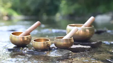 Tibetische Klangschalen mit Schlägeln auf Steinen im Fluss - Foto: Olga Yastremska/iStock