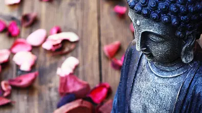 Buddha-Figur in Nahaufnahme mit Blütenblättern im Hintergrund - Foto: Extended License / AdobeStock