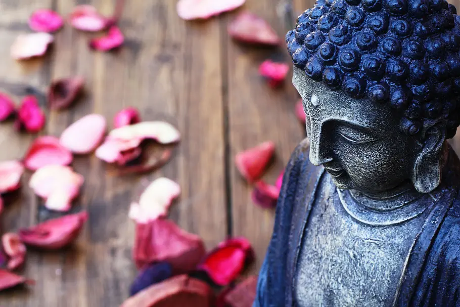 Buddha-Figur in Nahaufnahme mit Blütenblättern im Hintergrund