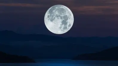 Vollmond steht bei Nacht über einem dunklen See - Foto: Onkamon / AdobeStock