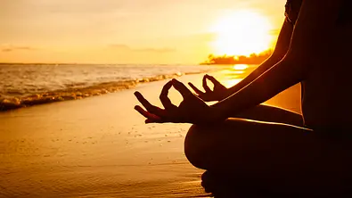 Jemand meditiert während dem Sonnenaufgang am Strand - Foto: iStock/kieferpix
