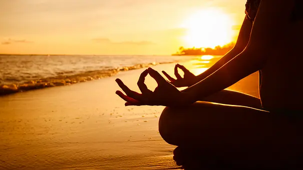 Jemand meditiert während dem Sonnenaufgang am Strand - Foto: iStock/kieferpix