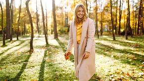Frau steht lächelnd in einem spätsommerlichen Wald - Foto: maxbelchenko / AdobeStock