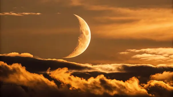 Ein leuchtender Neumond steht an einem goldenen Abendhimmel, umgeben von vielen Wolken - Foto: Platon/AdobeStock Ein leuchtender Neumond steht an einem goldenen Abendhimmel, umgeben von vielen Wolken - Foto: Platon/AdobeStock